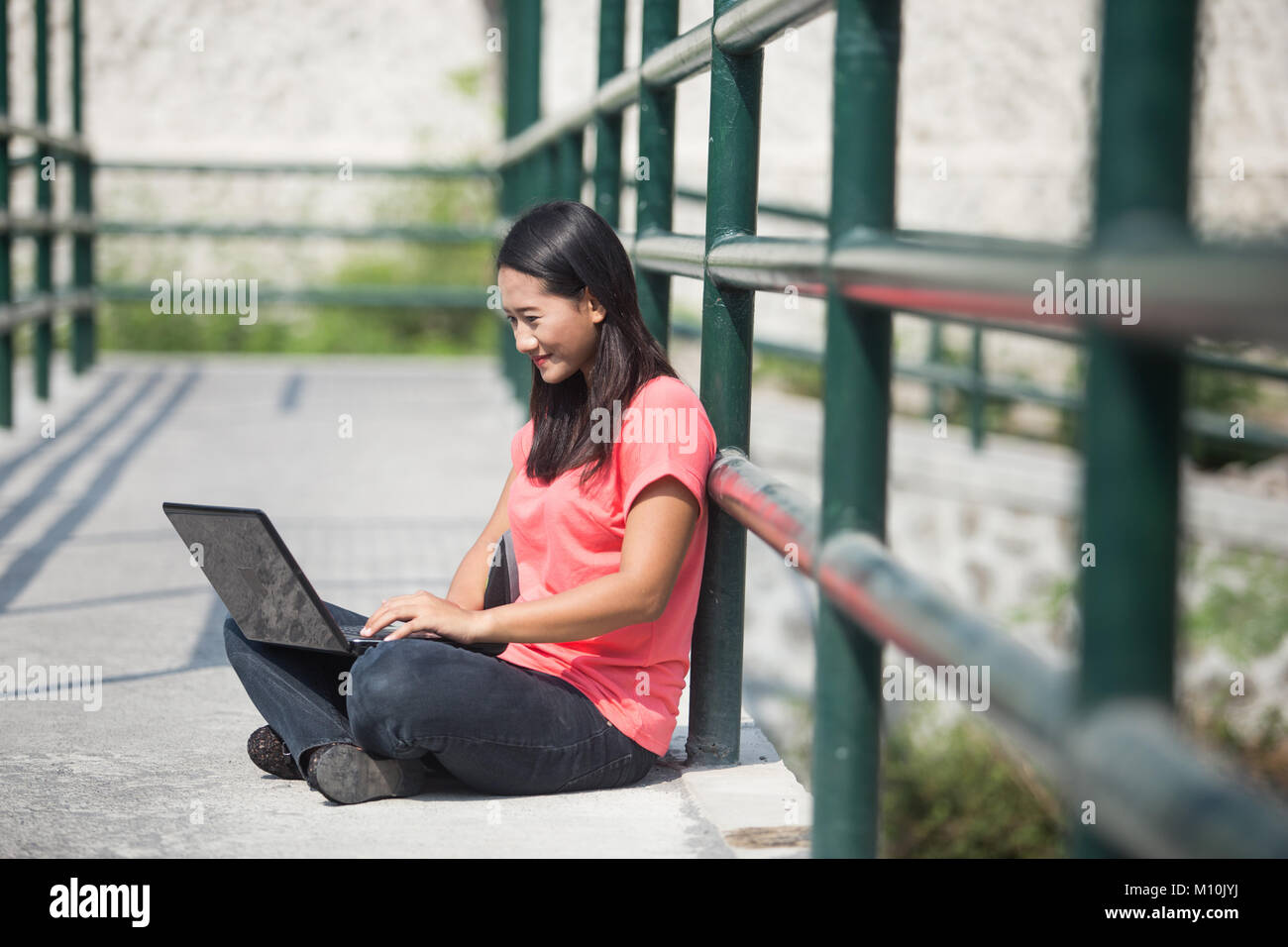 A portrait of a young Asian student sitting outdoor, using a laptop ...