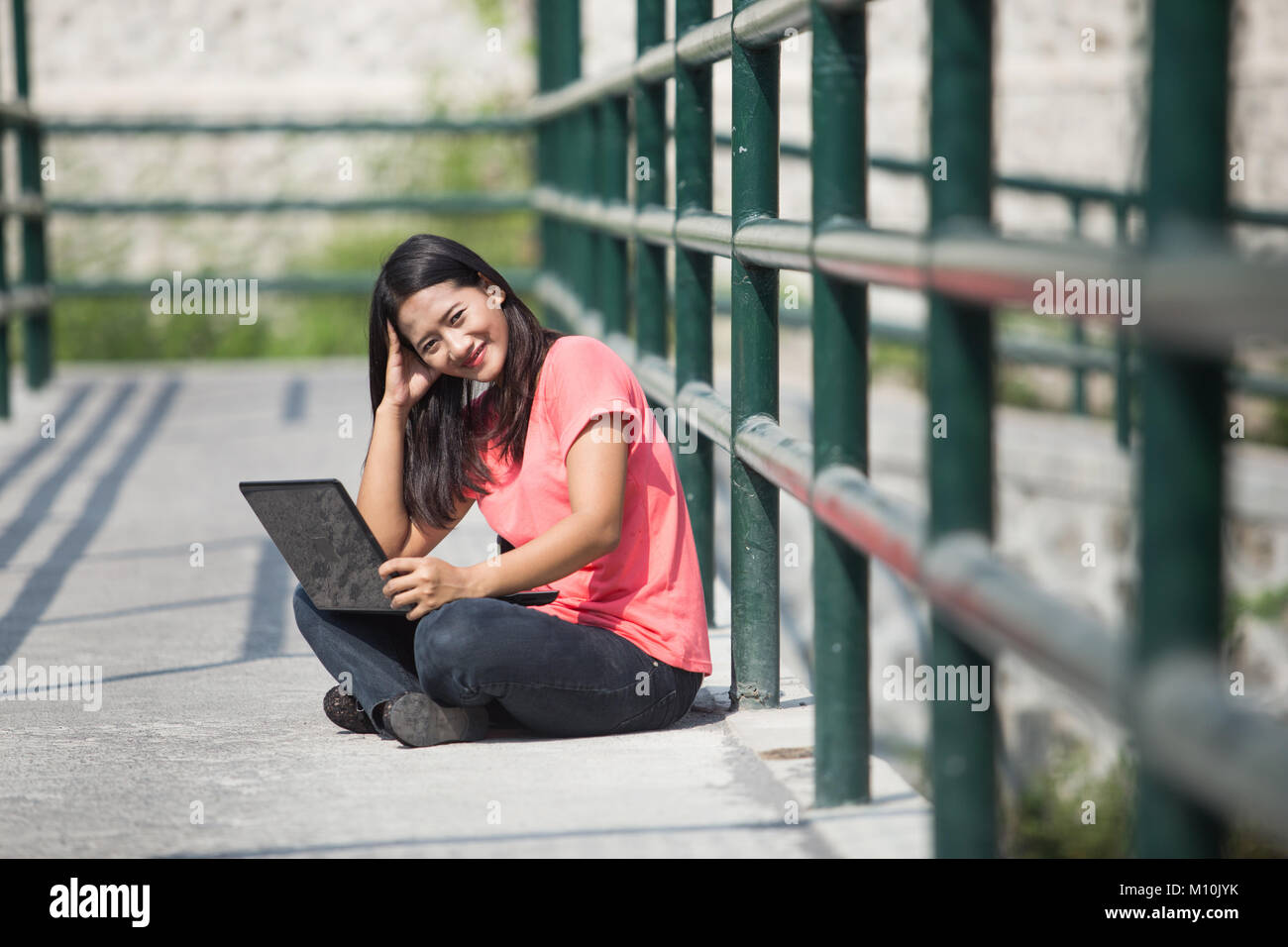 A portrait of a young Asian student sitting outdoor, with laptop and ...