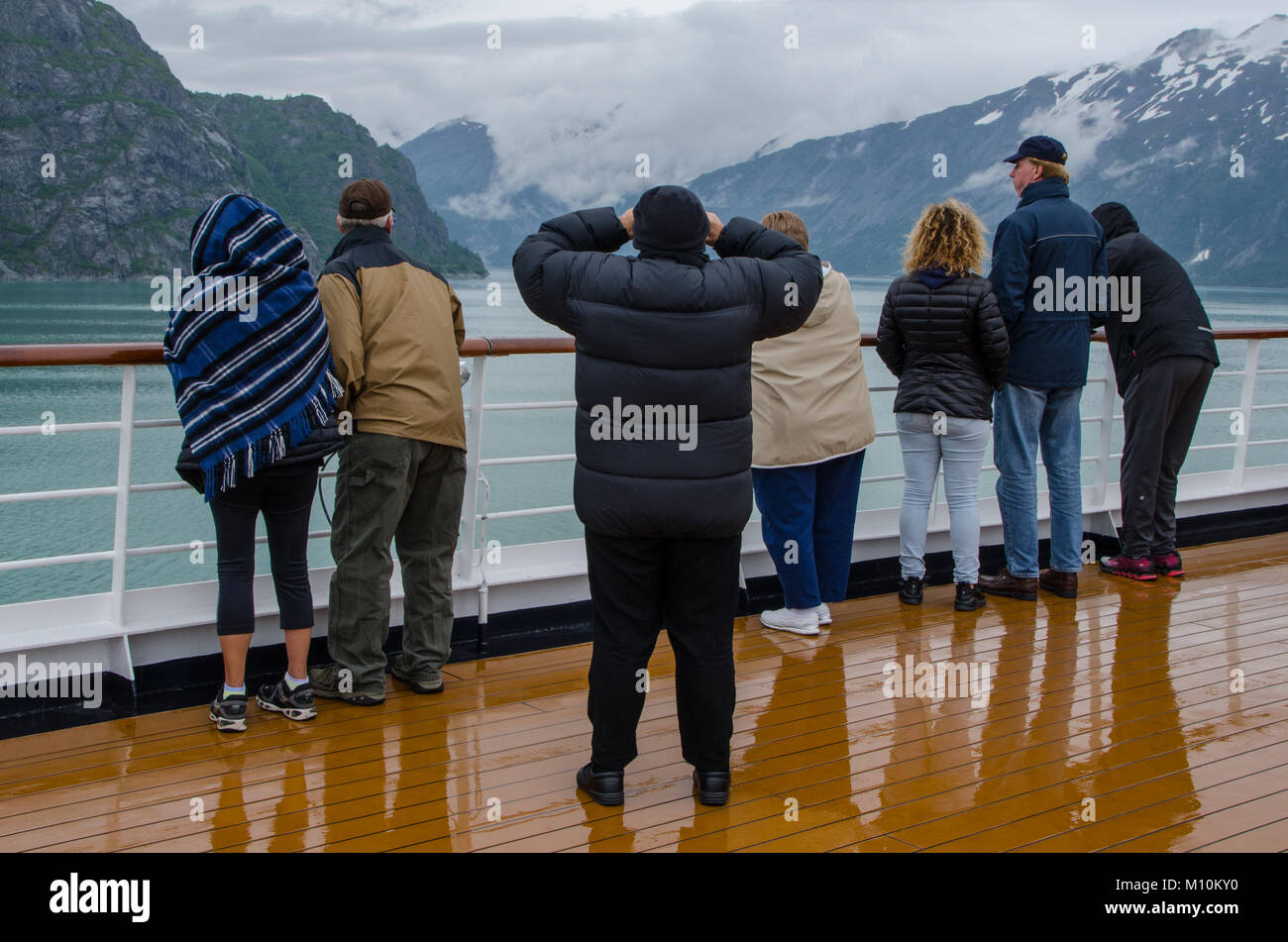 Small group of passengers standing by deck railing look out at scenic landscape on Alaska cruise - Glacier National Park, Alaska Stock Photo