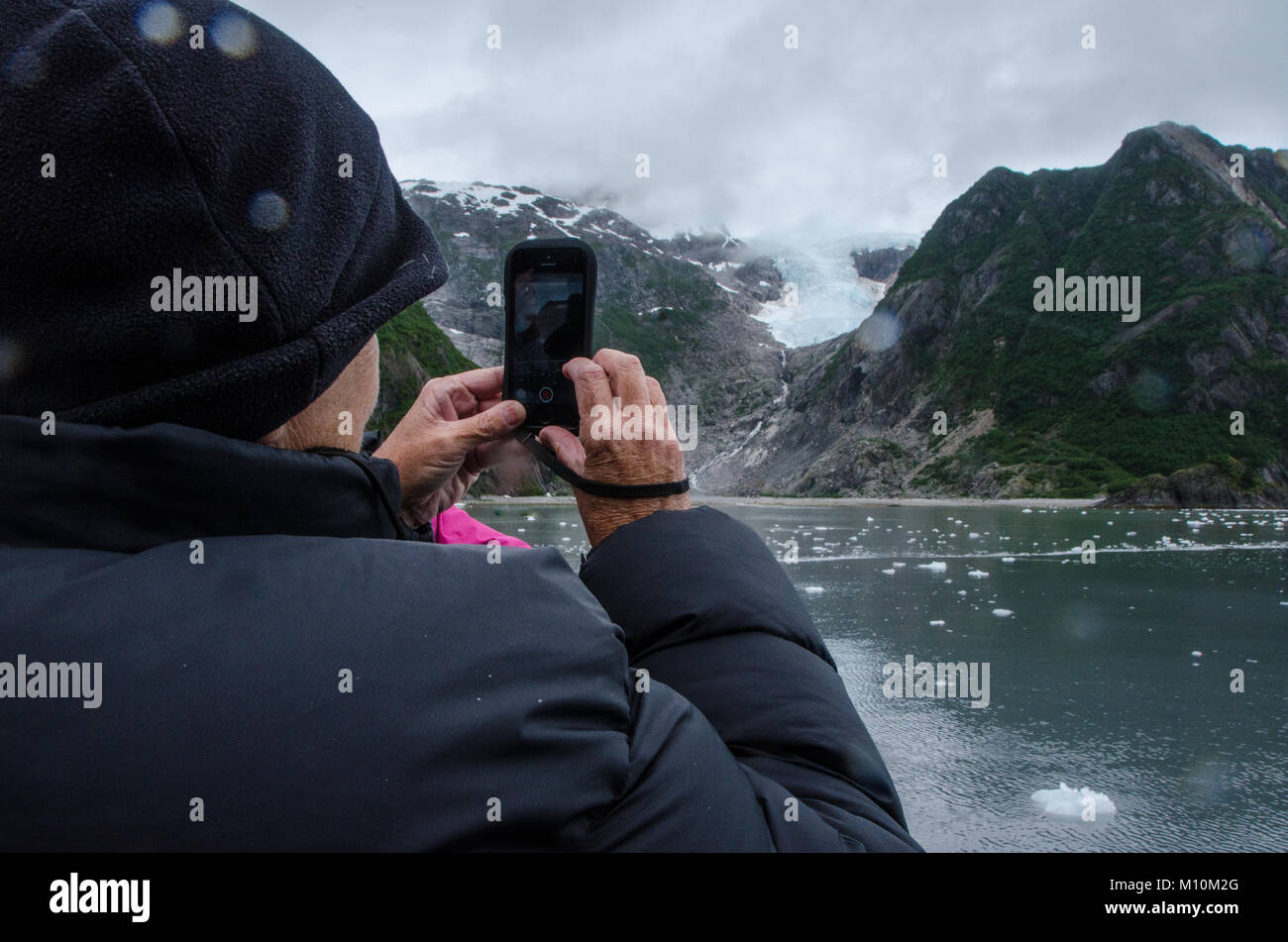 Mature passenger with smartphone takes photograph of glacier on Alaskan cruise - at Glacier Bay National Park, Alaska. Stock Photo