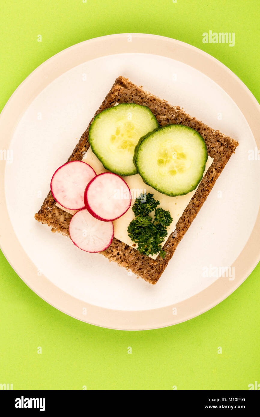 Cheese and Cucumber Open Face Rye Bread Sandwich With Radishes Against A Green Background Stock Photo