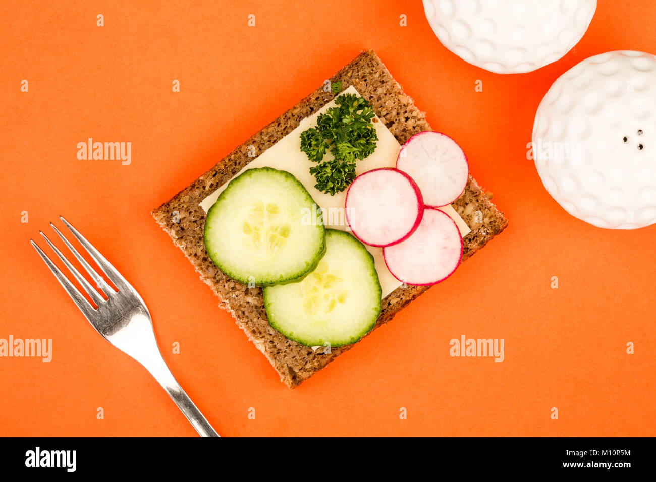 Cheese and Cucumber Open Face Rye Bread Sandwich With Radishes Against An Orange Background Stock Photo