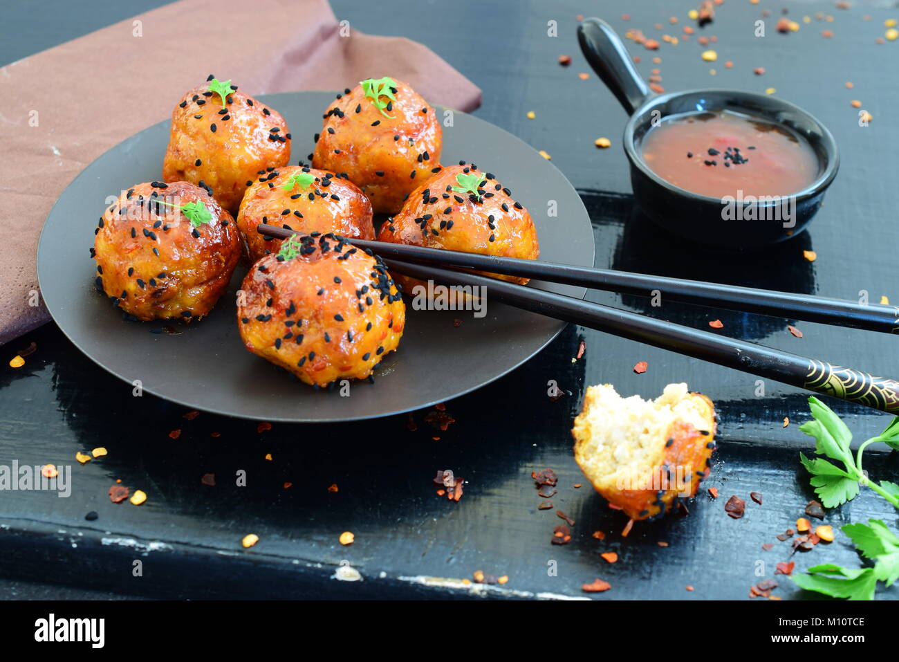 Spicy chicken balls in sweet chilli glaze on a metal tray on a black wooden background Stock Photo