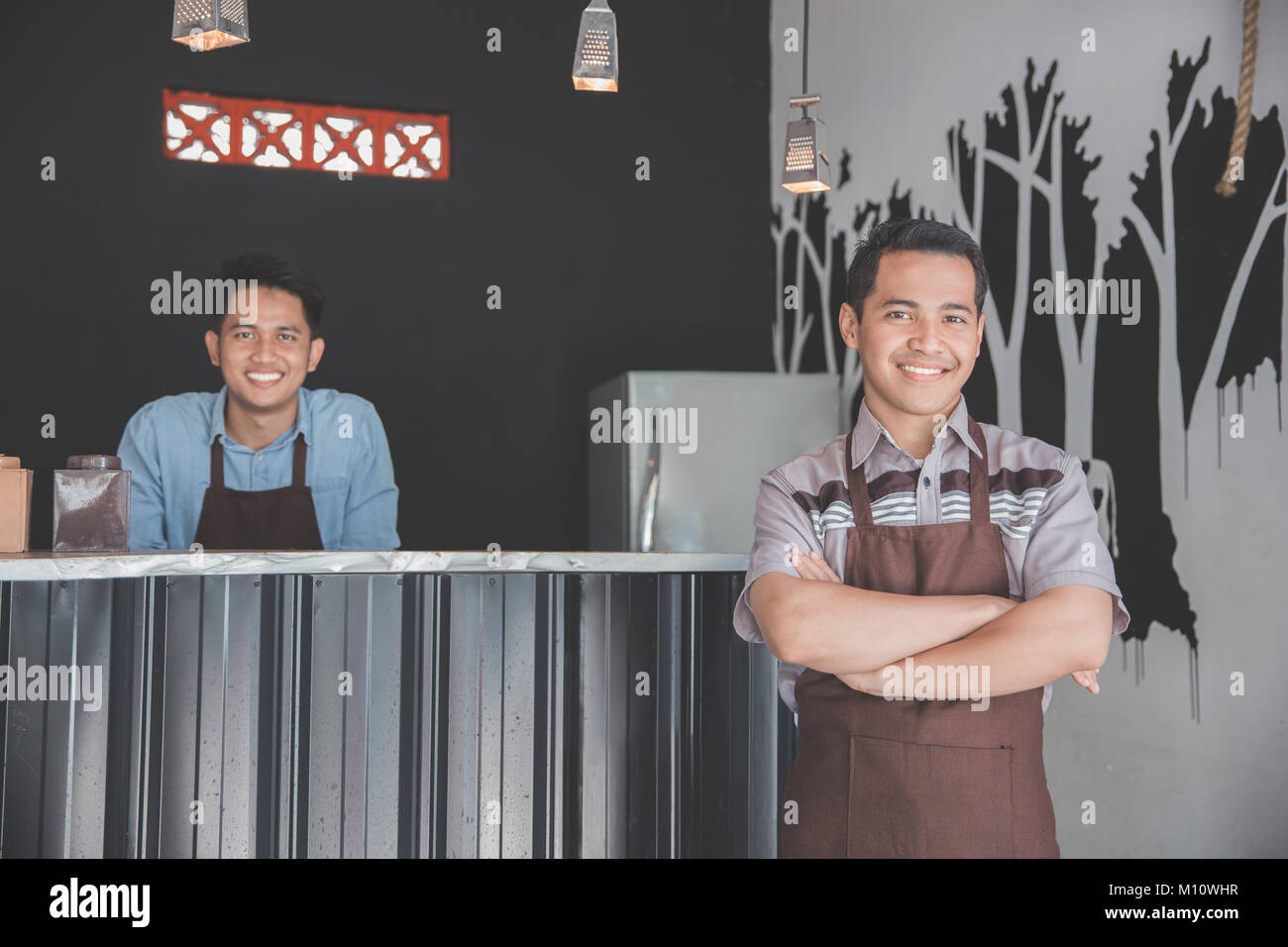 Successful coffee shop owner standing with crossed arms with partner at