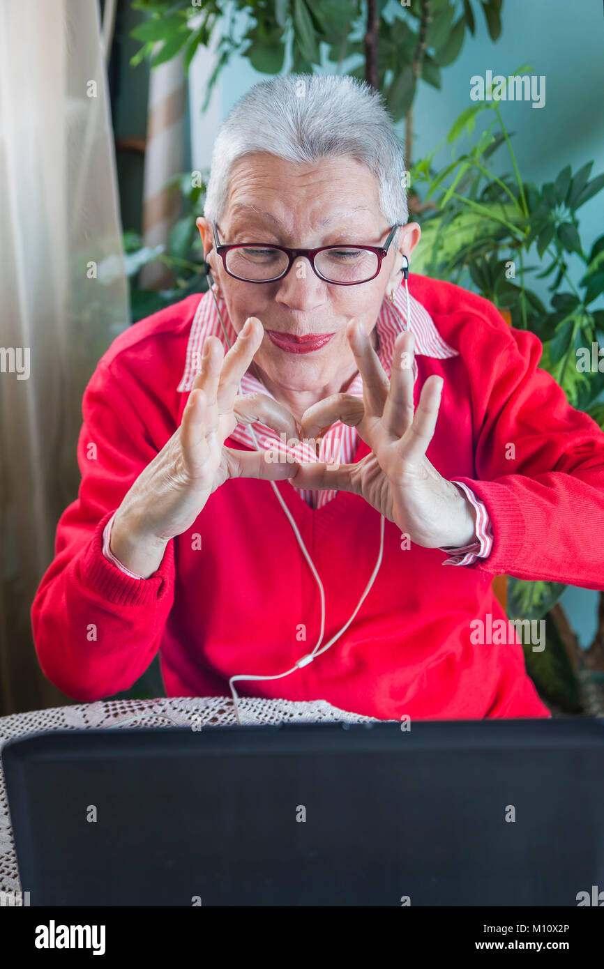 Grandma using laptop, camera and earphones for distant connections Stock Photo