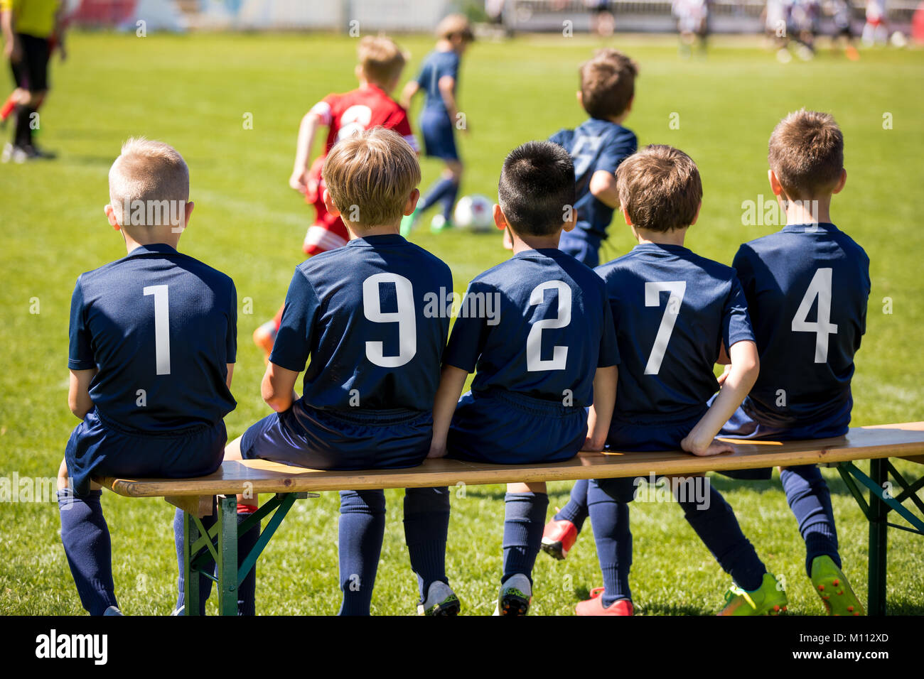 Young boys watching soccer competition from bench. Soccer players under 10 years old. Kids football club players in blue jersey Stock Photo