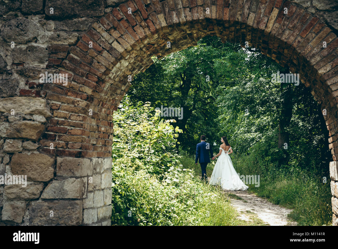 Back view of the beautiful walking newlywed couple by the hand along ...