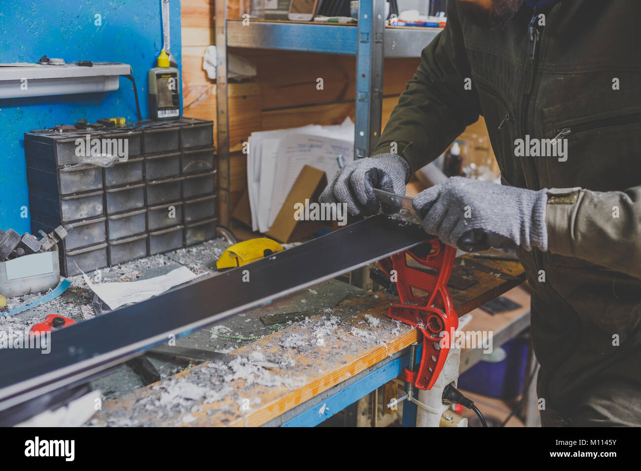 A male worker in a ski service repairs the sliding surface of