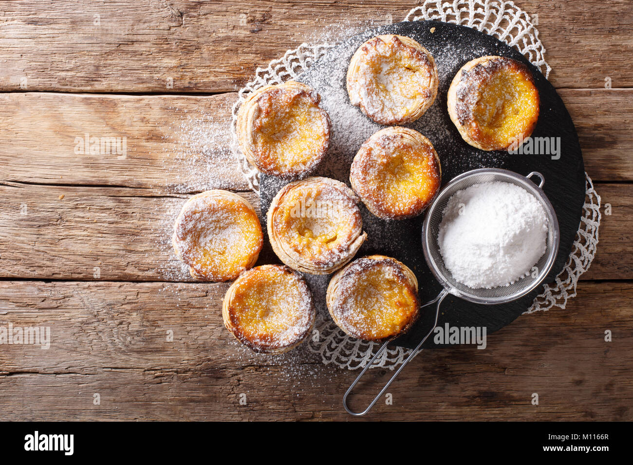 Fresh pastry dessert Pastel de nata with custard, sprinkled with powdered sugar close-up on the table. Horizontal top view from above Stock Photo