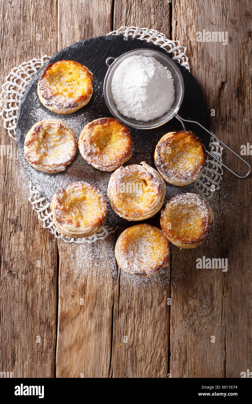 Fresh pastry dessert Pastel de nata with custard, sprinkled with powdered sugar close-up on the table. Vertical top view from above Stock Photo