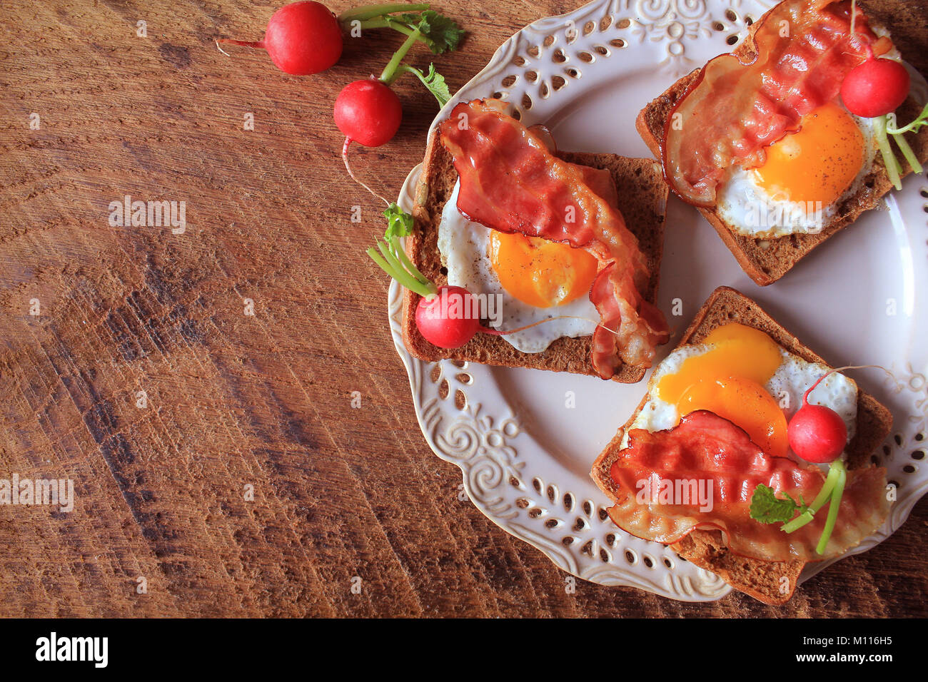 Breakfast , crispy bacon, fried eggs and bread. Sandwiches on white plate. Rustic table . Top