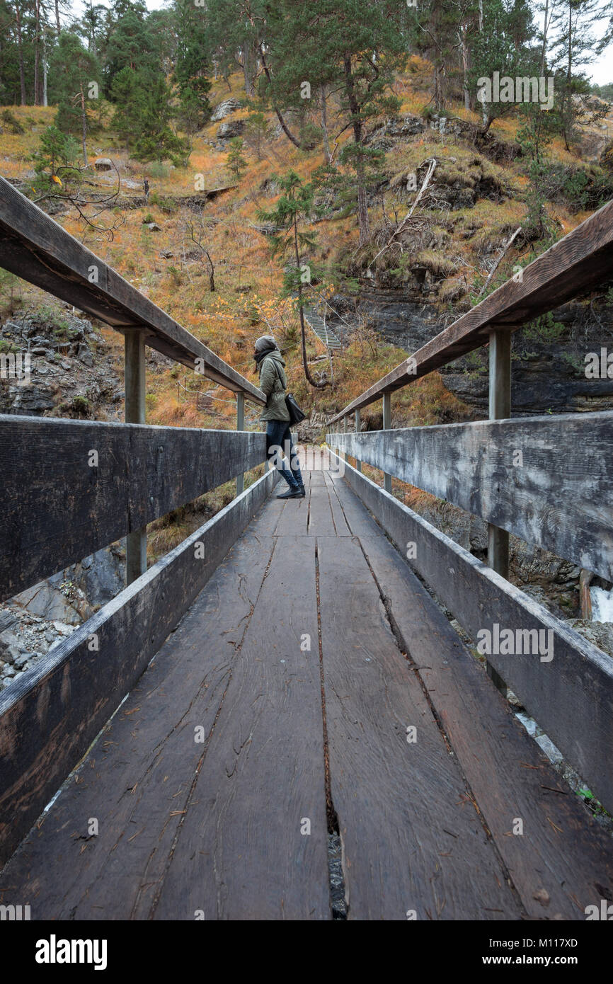 Woman standing on a bridge at the german waterfall - Kuhfluchtwasserfall - near the german alps while autumn. Vertical. Stock Photo