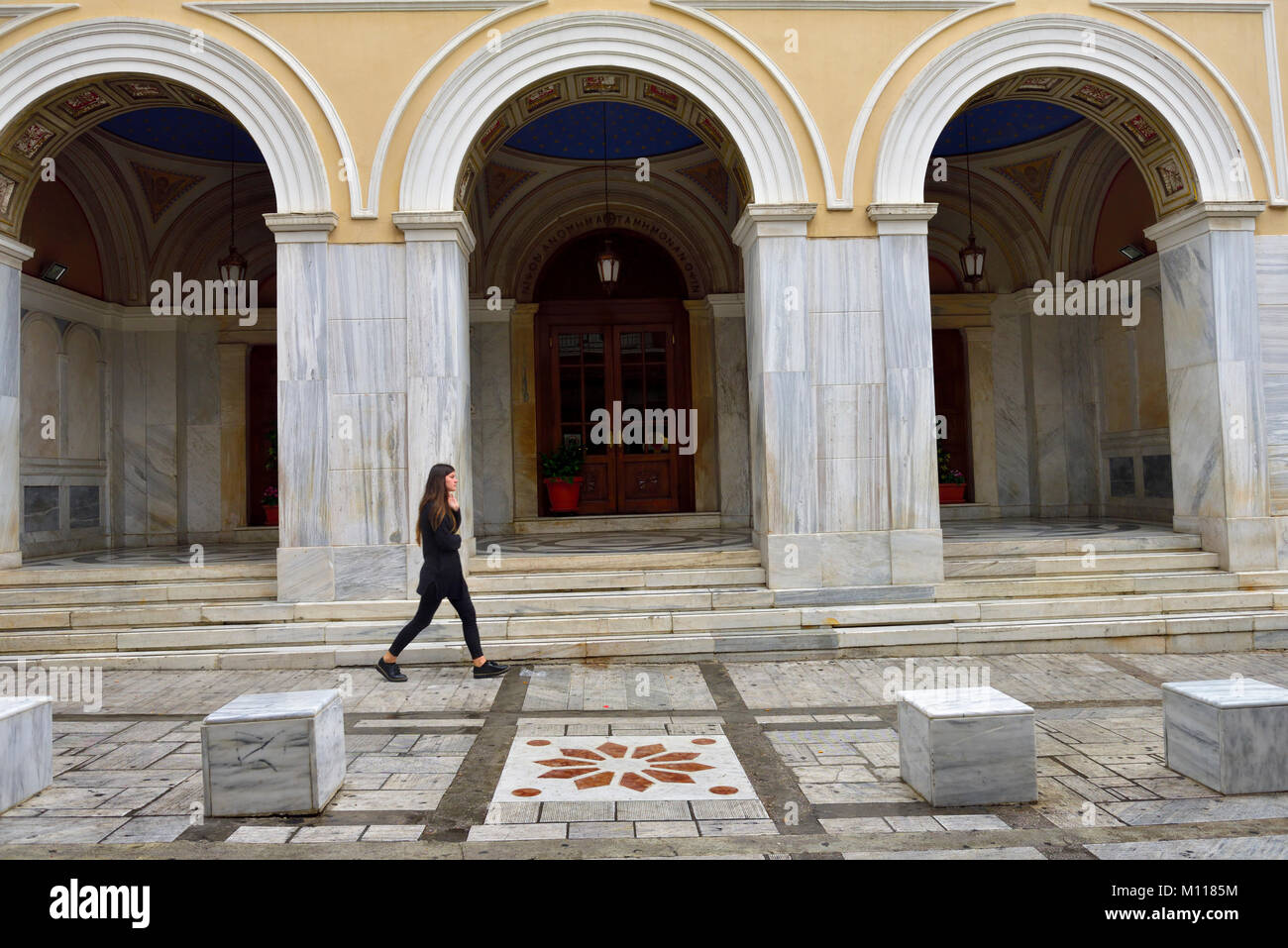 Lone young woman walking in front of building doors, marble pillars of Church St. Irene or Agia Irini, Athens Stock Photo