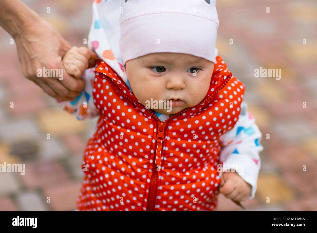 little girl learns to walk, taking its first steps. Female hands mother support the child. autumn Stock Photo