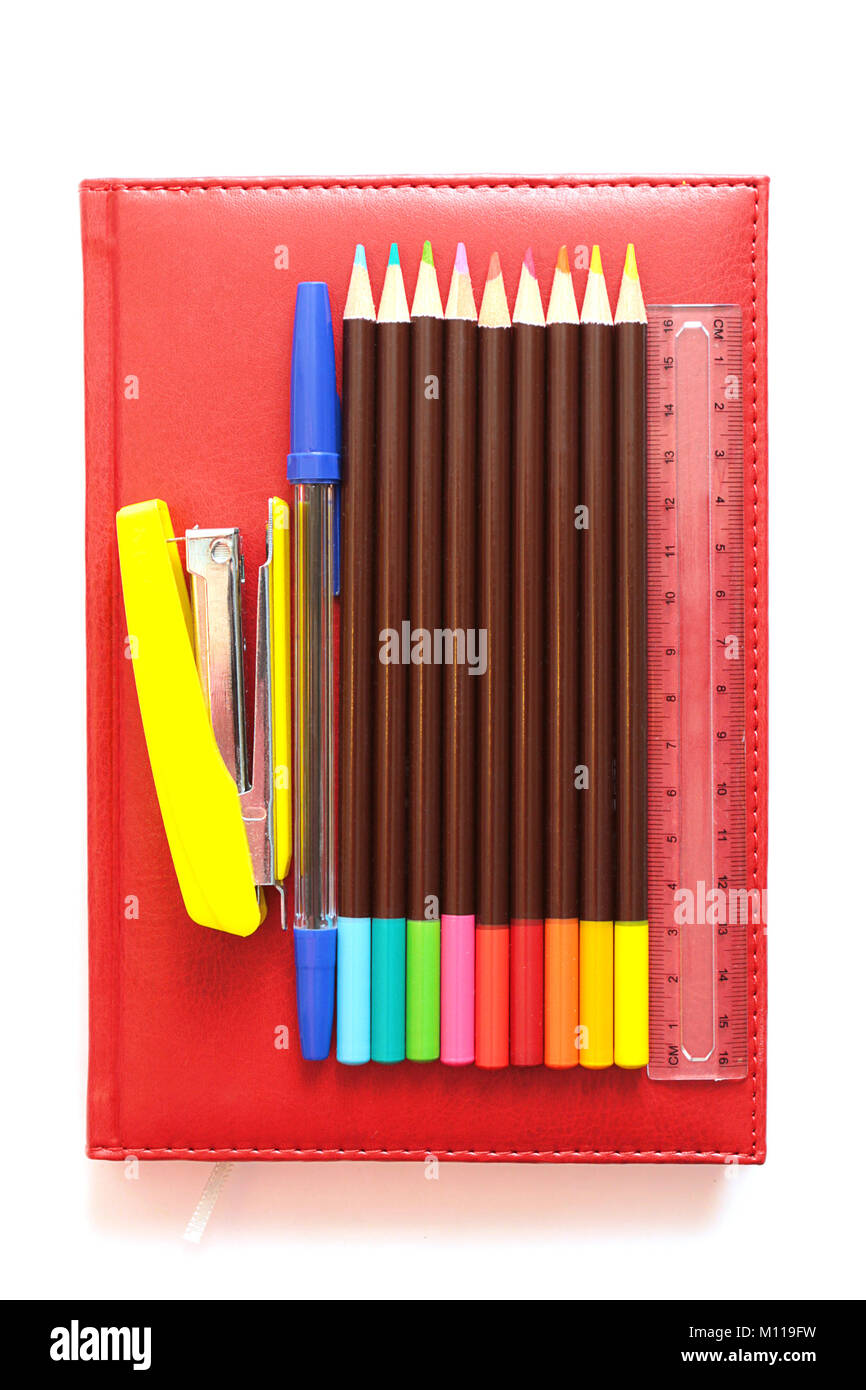 Yellow stapler, pen, ruler, colored pencils on a red diary Stock Photo