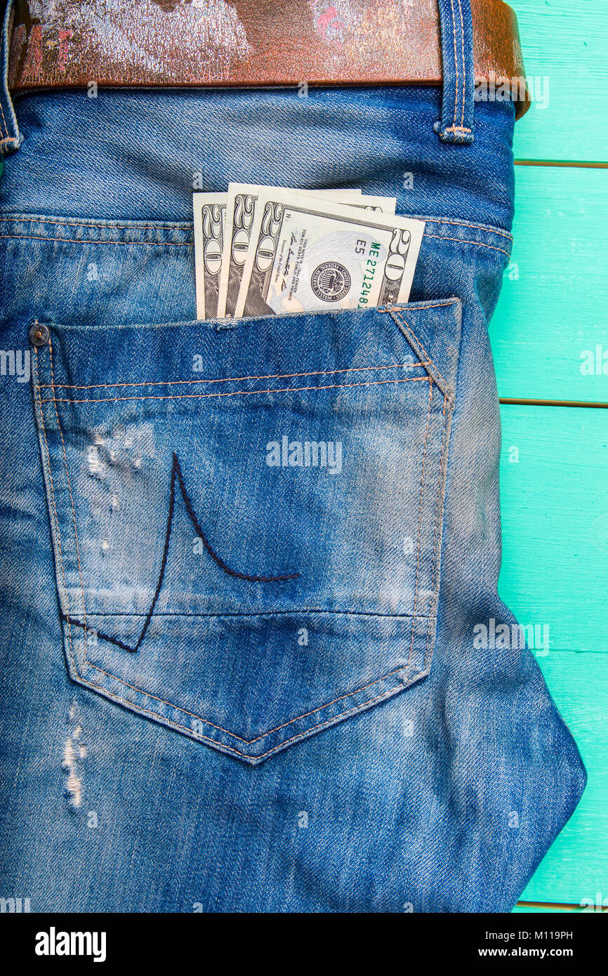 $ 20 bill in the pocket of jeans, jeans neatly stacked on wooden background, top view Stock Photo