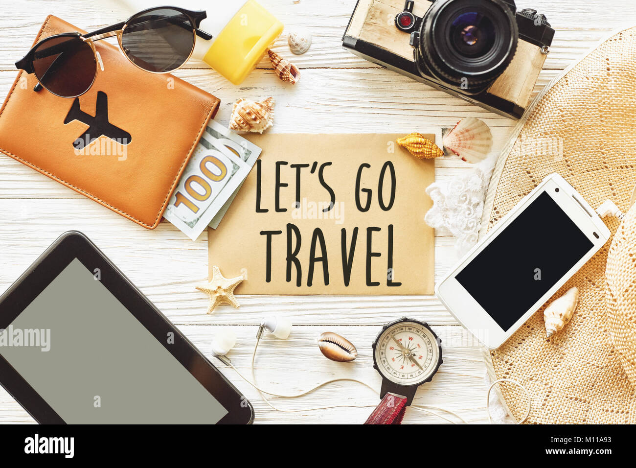 travel. let's go travel text sign concept on card flat lay, camera sunglasses compass passport money phone hat shells on white wooden background top v Stock Photo