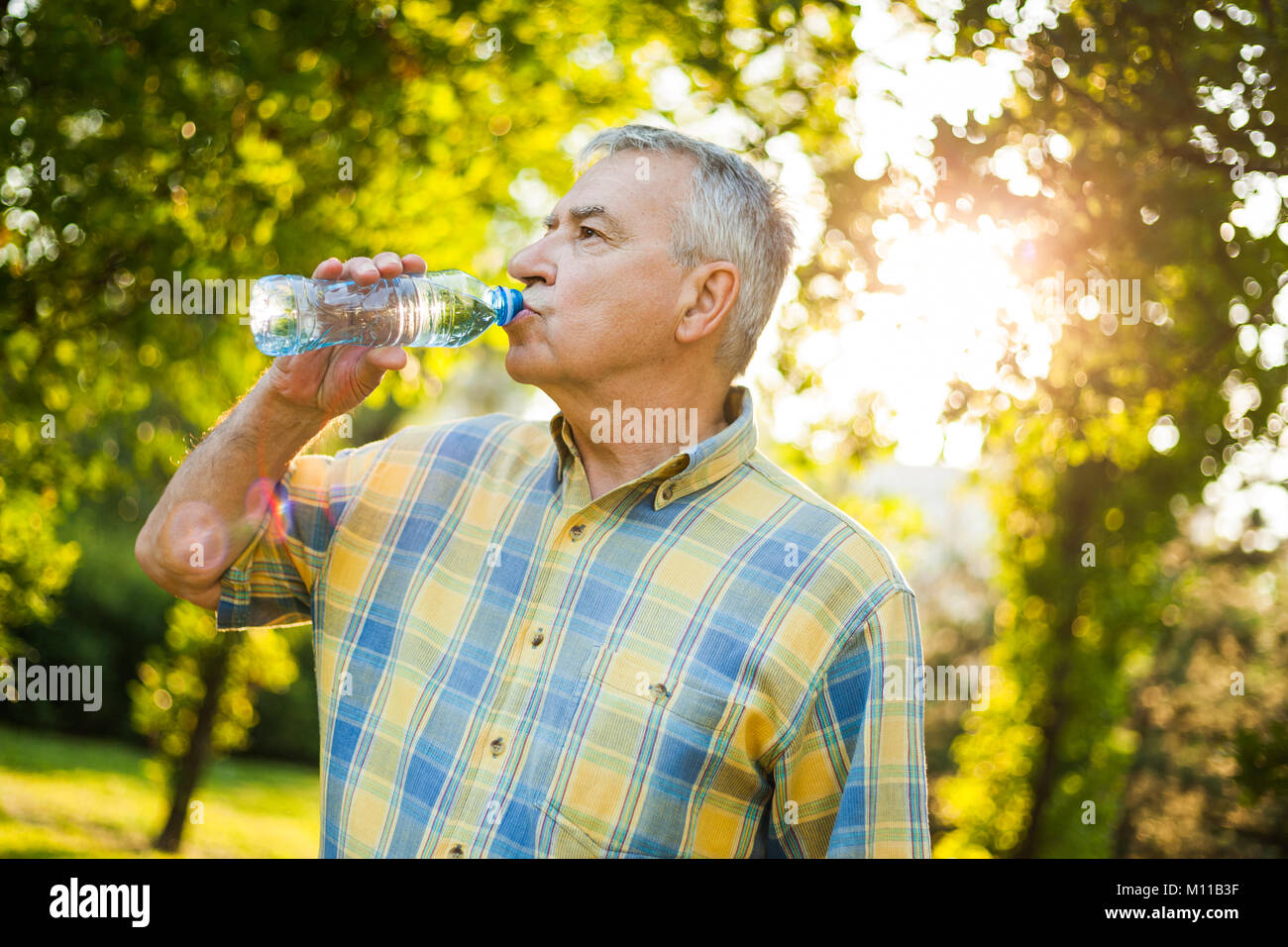 Senior man is drinking water in park Stock Photo - Alamy