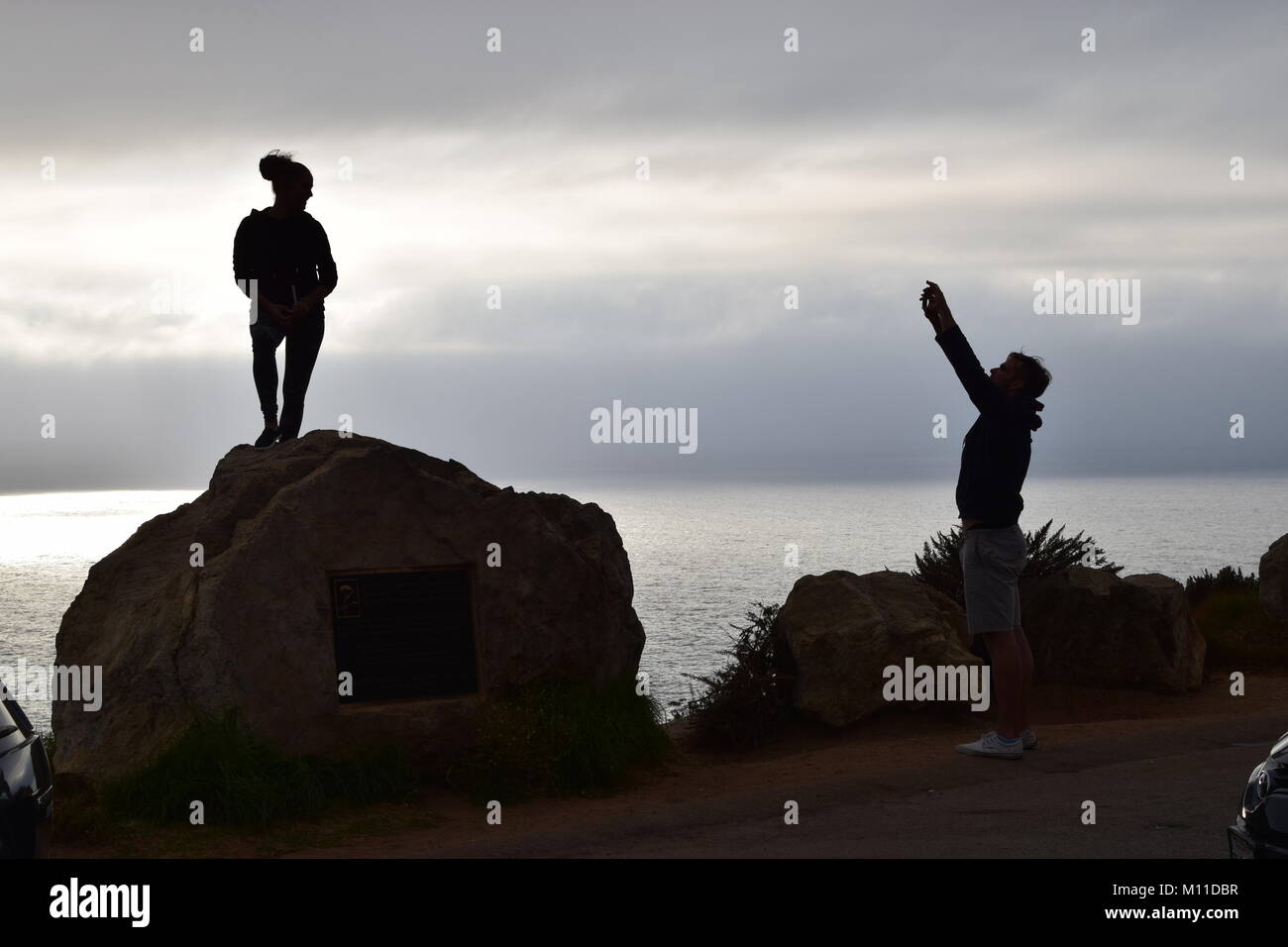 Silhouette of young couple taking photo on Highway 1, Big Sur, California Stock Photo