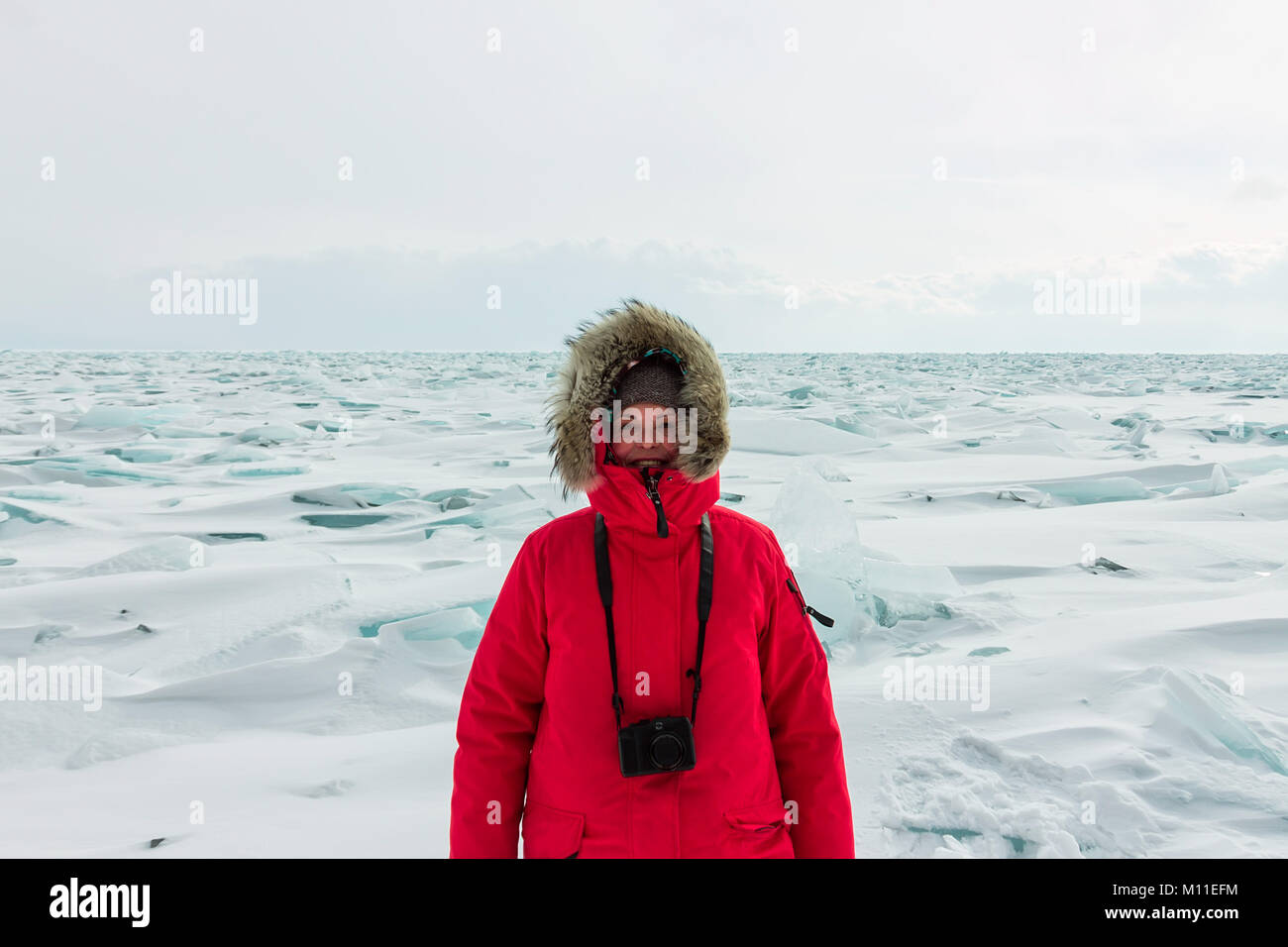 Portrait of a woman in a parka jacket with a fur hood in a snowy Baikal in hummocks. Stock Photo