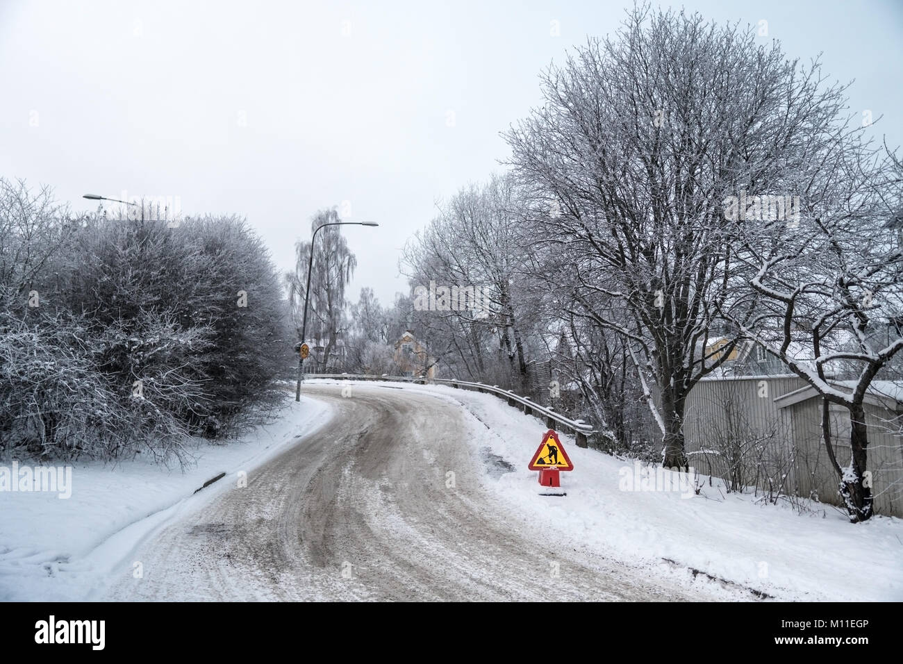 Under construction road sign on a winter day in a city. Snow and frozen trees and nearby houses in a residential area in Sweden Stock Photo