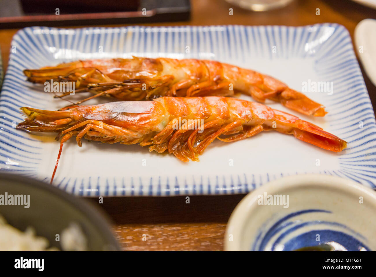 Two fully cooked grilled shrimps on a white plate, served along with many other Japanese dishes Stock Photo