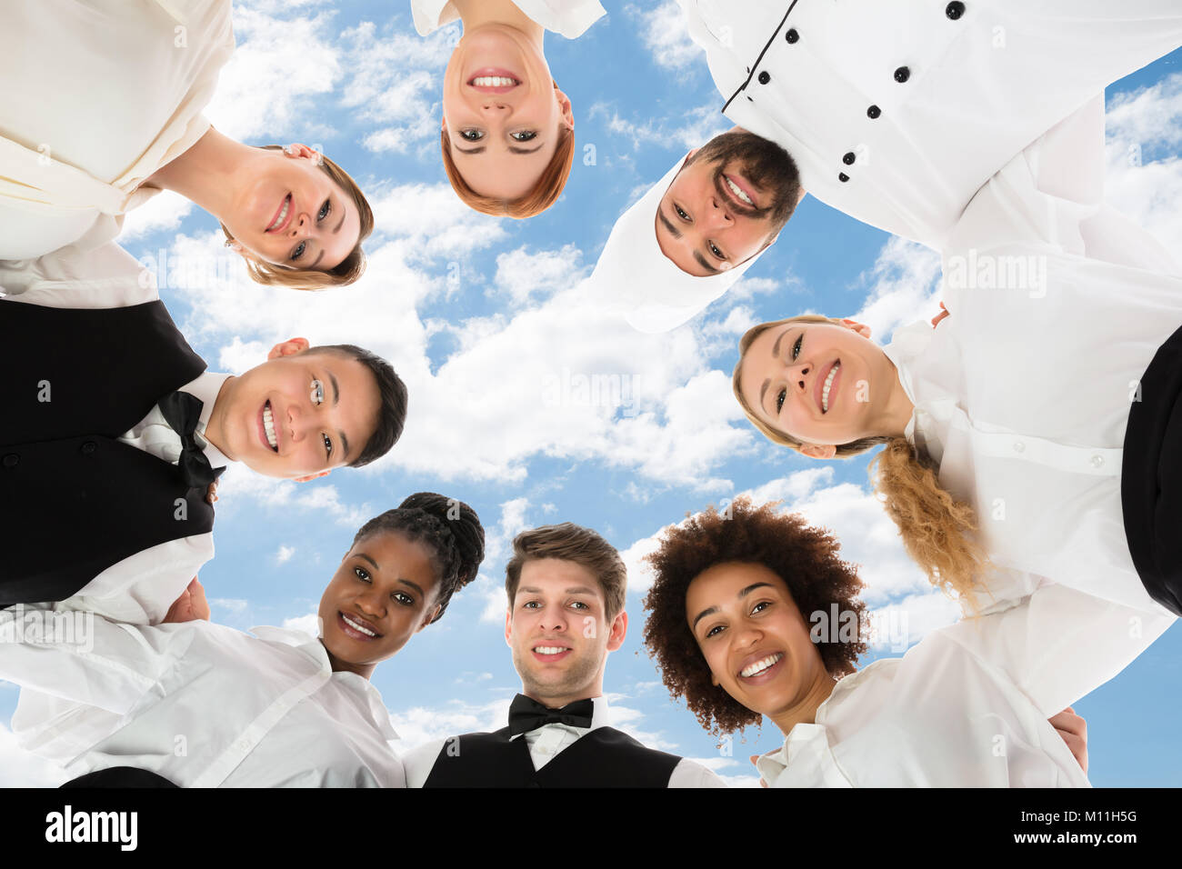 Smiling Restaurant Staff Forming Huddle Against Cloudy Sky Stock Photo