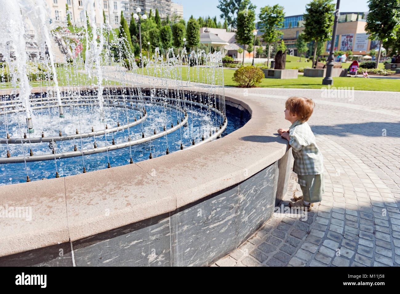 Three years old child in the park with water fountain and blue sky Stock Photo