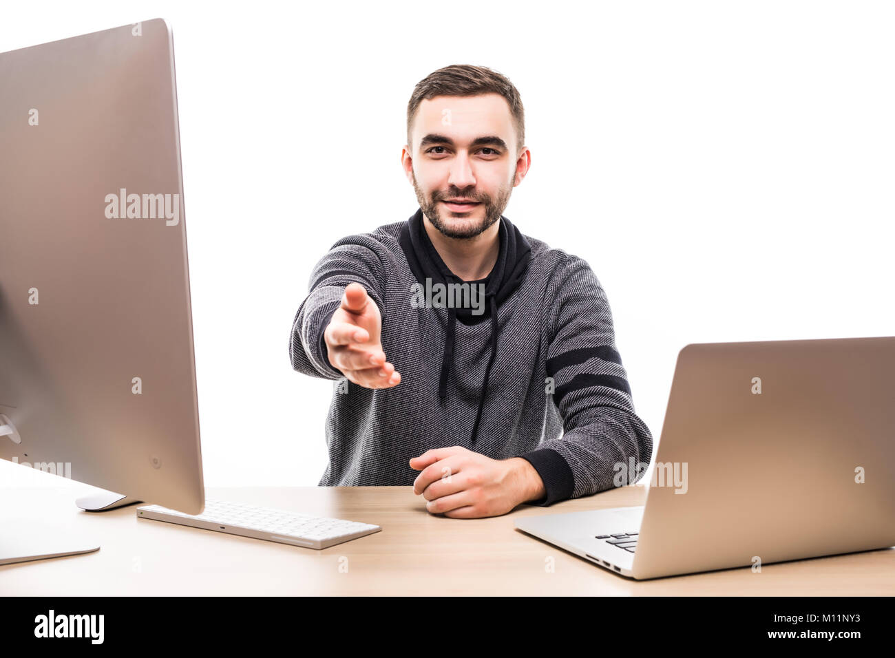Young man with pc and laptop bidding you at his desk isolated