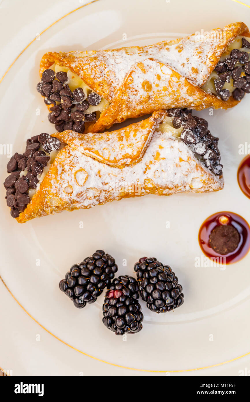 Italian cannoli on white plate with blackberries and chocolate chips