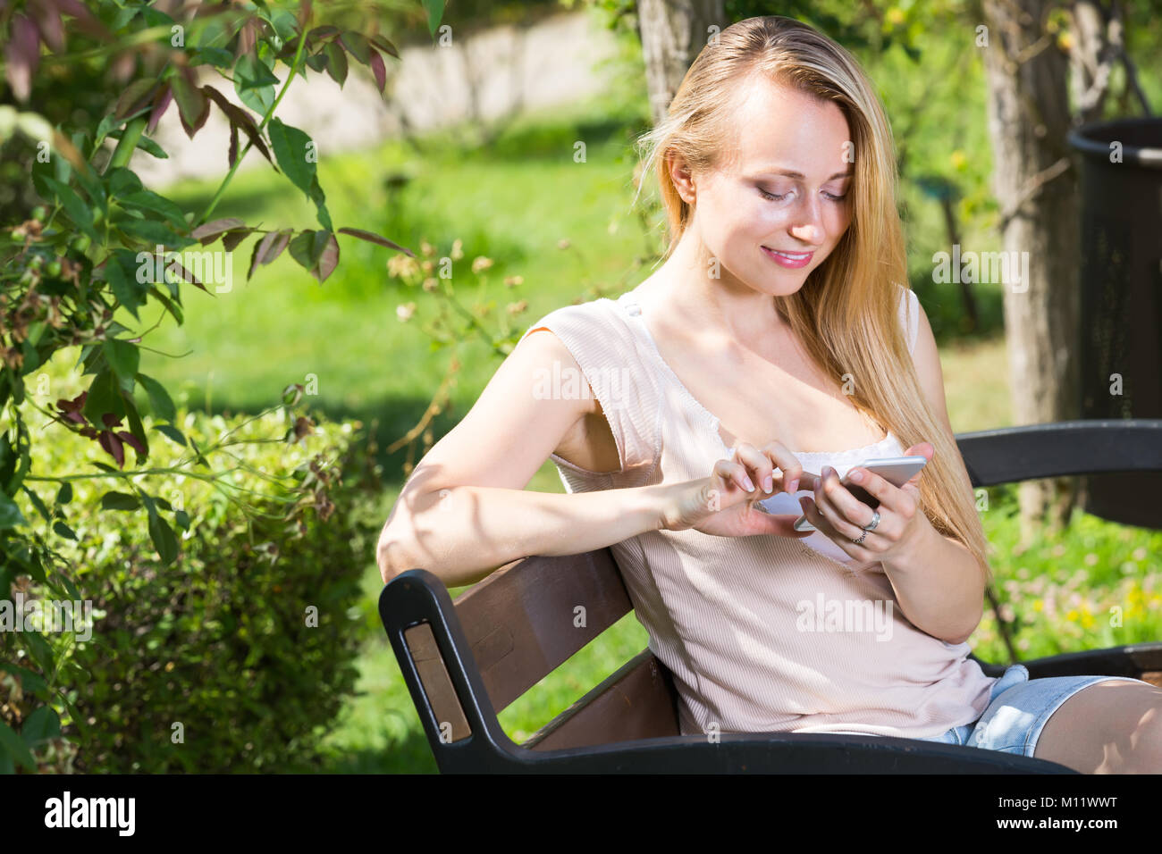 Portrait of cheerful smiling young woman sitting on bench and looking ...