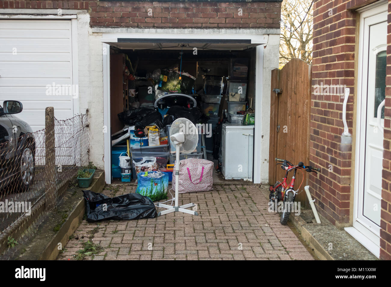 Looking down a residential driveway at an open garage which is filled with clutter and belongs kept in storage inside. Stock Photo