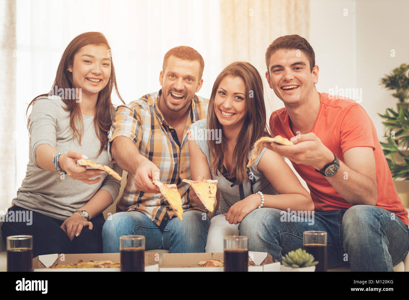 Four cheerful friends hanging out in an apartment. They are eating ...