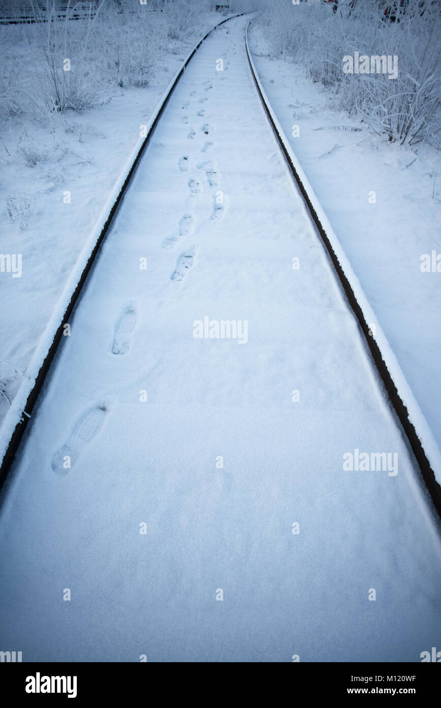 Railroad tracks in winter with foot steps on snow leading forward Stock Photo