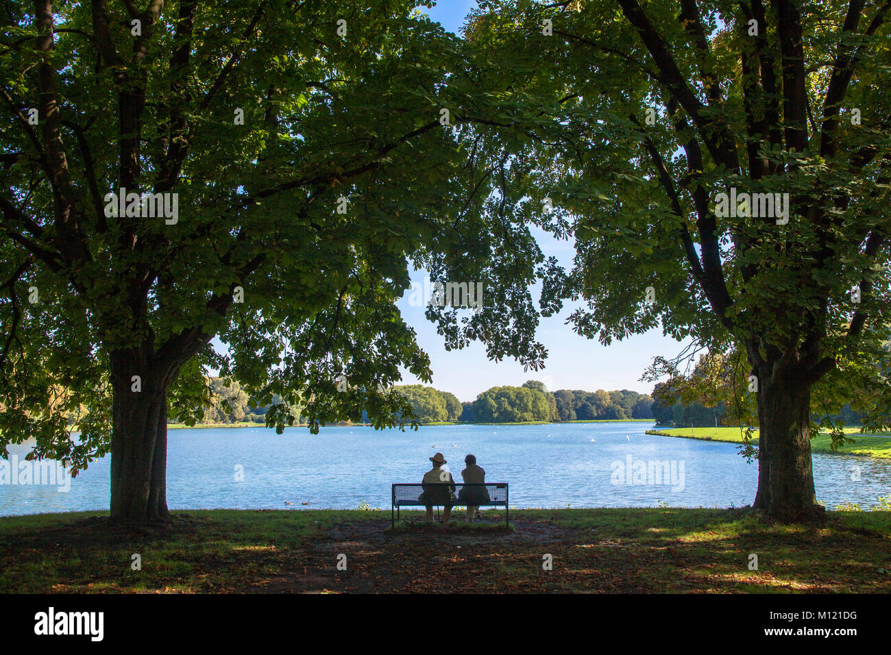 Germany, Cologne, couple on a bench in the town forest at pond Deckstein.  Deutschland, Koeln, Paar auf einer Bank am Decksteiner Weiher im Stadtwald. Stock Photo