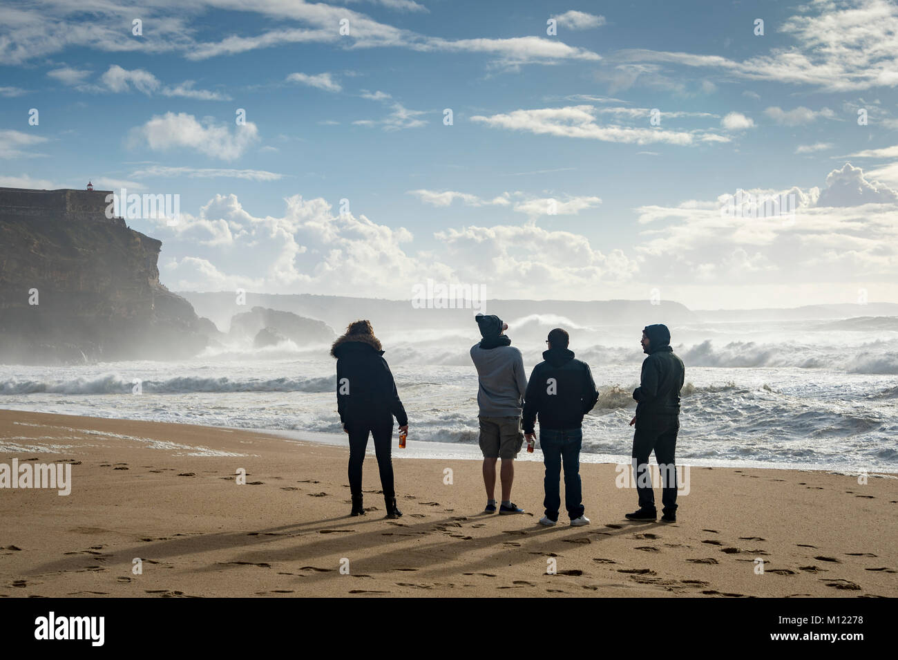 a group of four people watching the big waves at Praia do Norte, Nazare, Portugal. Stock Photo