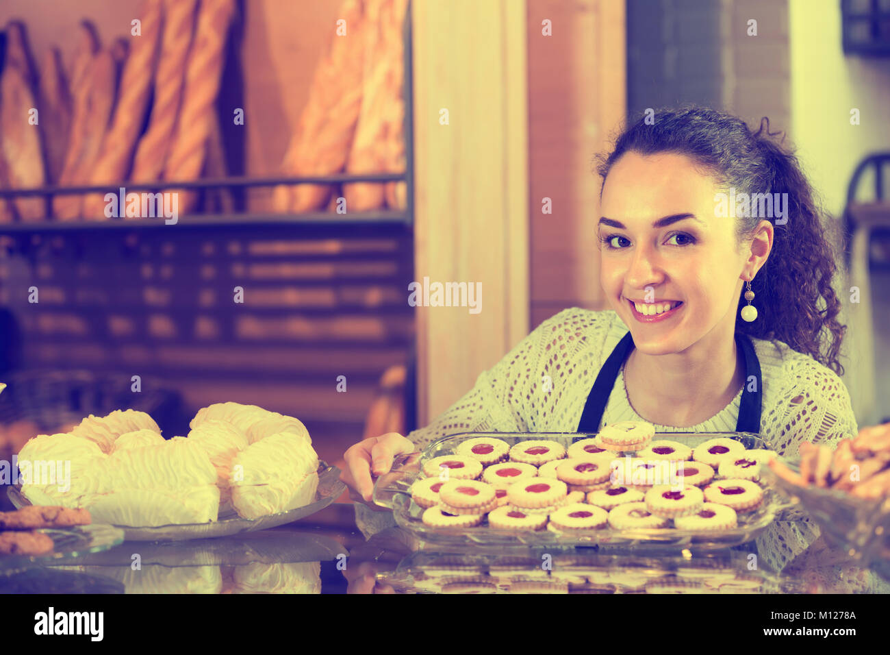 Hospitable girl with delicious cream pies at bakery display Stock Photo