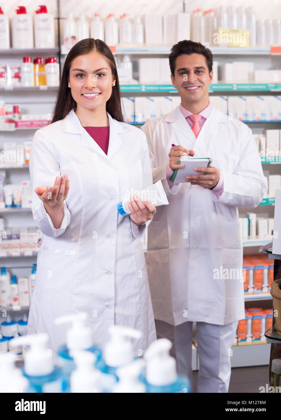 Two friendly smiling pharmacists in white uniform at the work in modern
