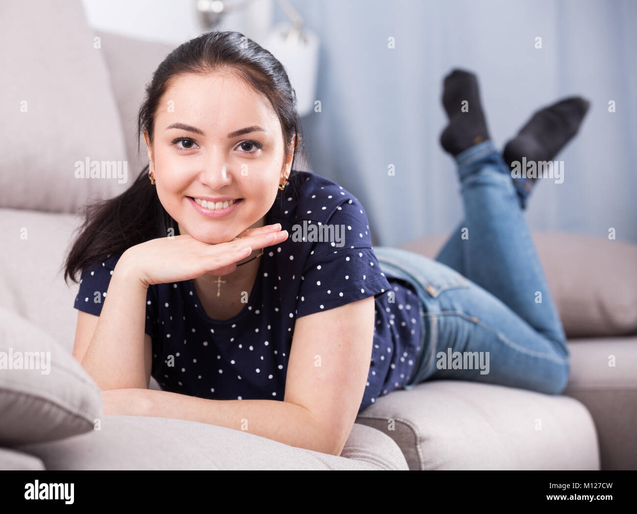 Young browneyed girl with smile leaning on fists on couch Stock Photo