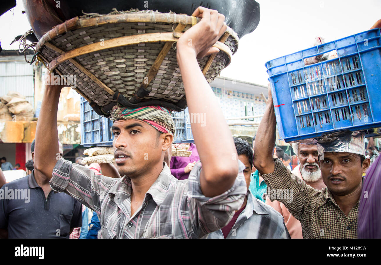 men at a fish market, carrying baskets of fish on their heads Stock Photo