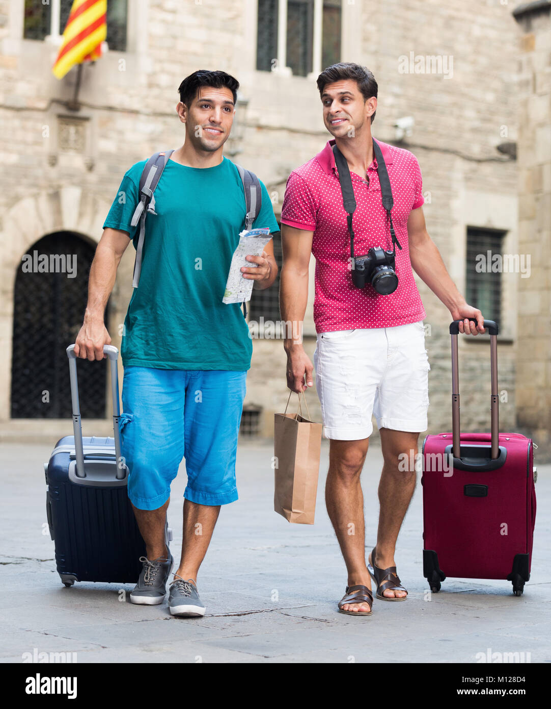 Two men are walking with baggage and map in Barcelona and watching to ...