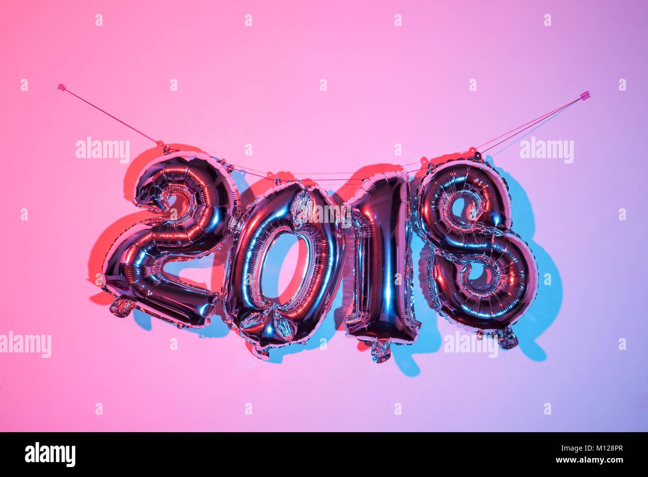 some fuchsia number-shaped balloons forming the number 2018, as the new year, hanging on a pink wall, with a stroboscopic effect Stock Photo