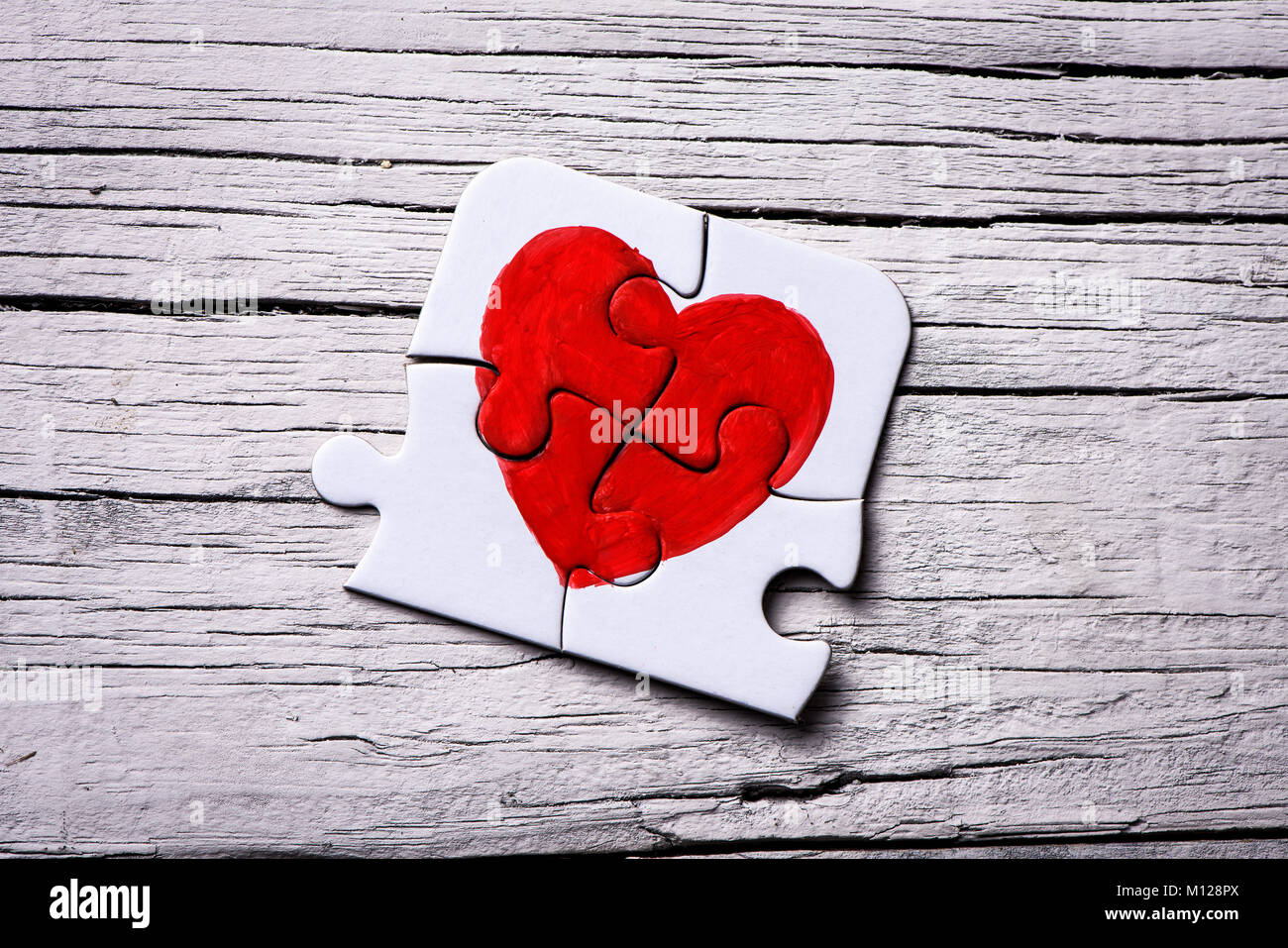 closeup of some pieces of a puzzle forming a heart on a white rustic wooden surface Stock Photo