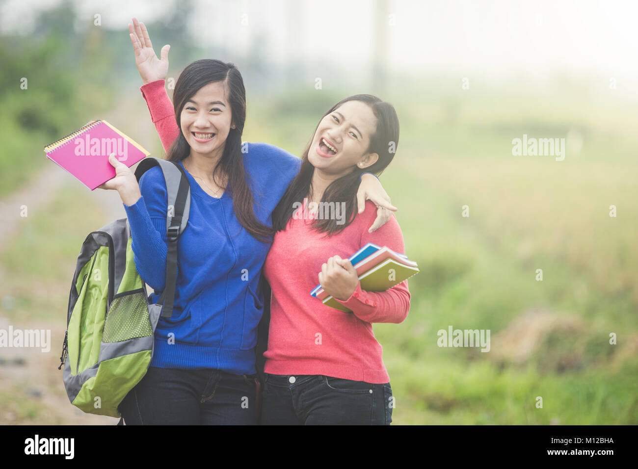 A portrait of two young Asian students holding books, smiling brightly ...