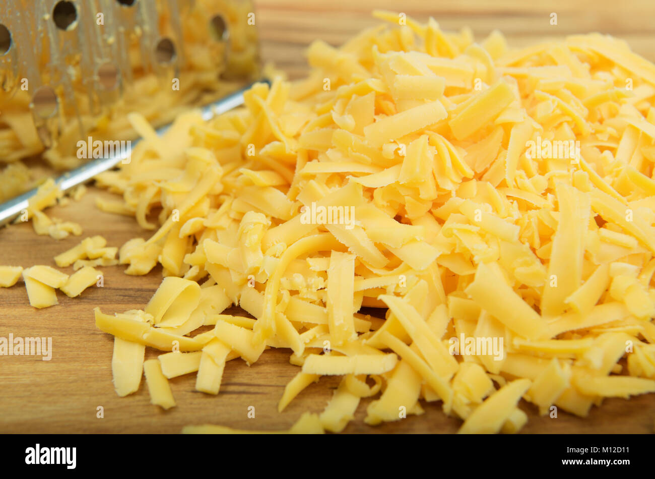 https://c8.alamy.com/comp/M12D11/close-up-detail-yellow-grated-cheese-hand-grater-on-wooden-board-food-M12D11.jpg