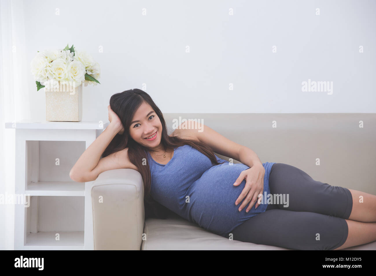 A portrait of a Beautiful Asian Pregnant woman laying on a couch Stock