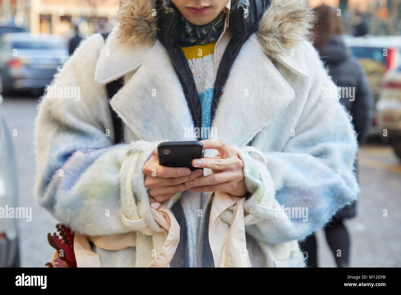 MILAN - JANUARY 14: Man with soft jacket in white and pale blue colors looking at phone before Daks fashion show, Milan Fashion Week street style on J Stock Photo