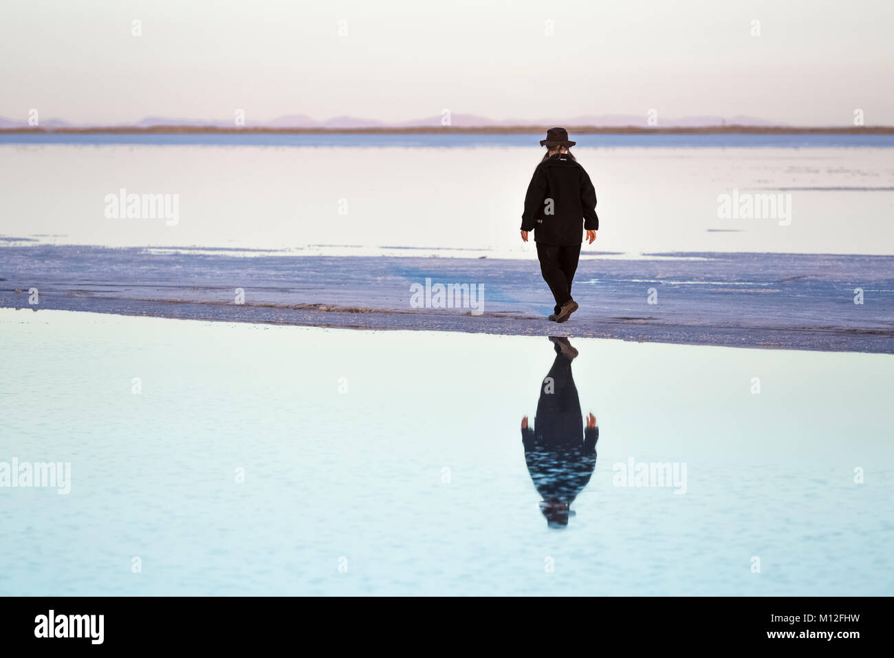Woman walking on a spit of land extending out into shallow salt water ...