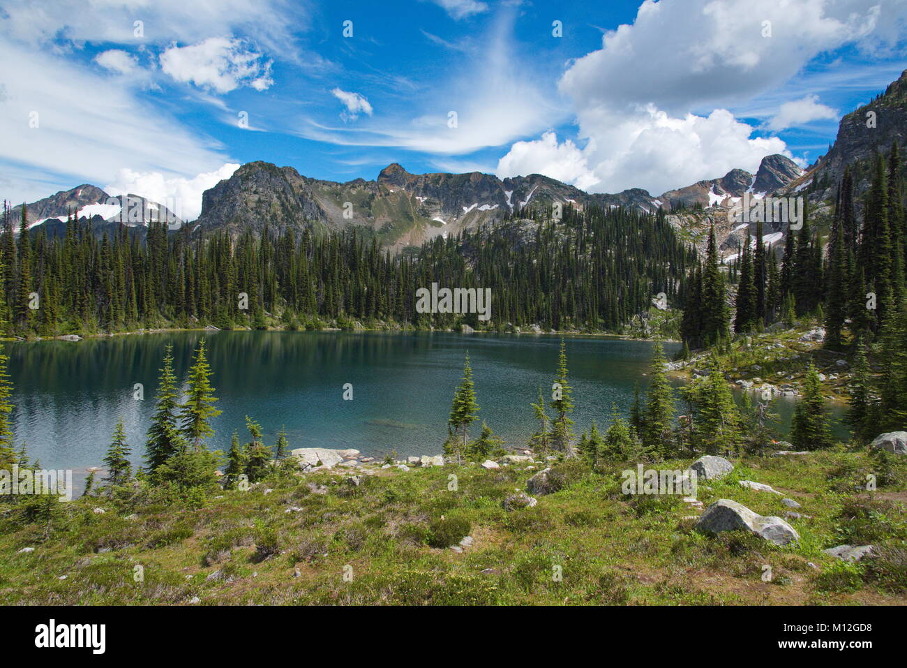 Summer view of Eva Lake with interesting clouds and deep blue sky.  Some snow on the mountains in the background. Stock Photo