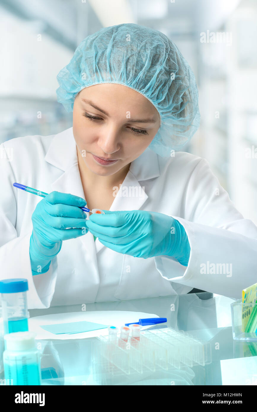 Young female scientist or tech labels test tubes for experiment in laboratory Stock Photo